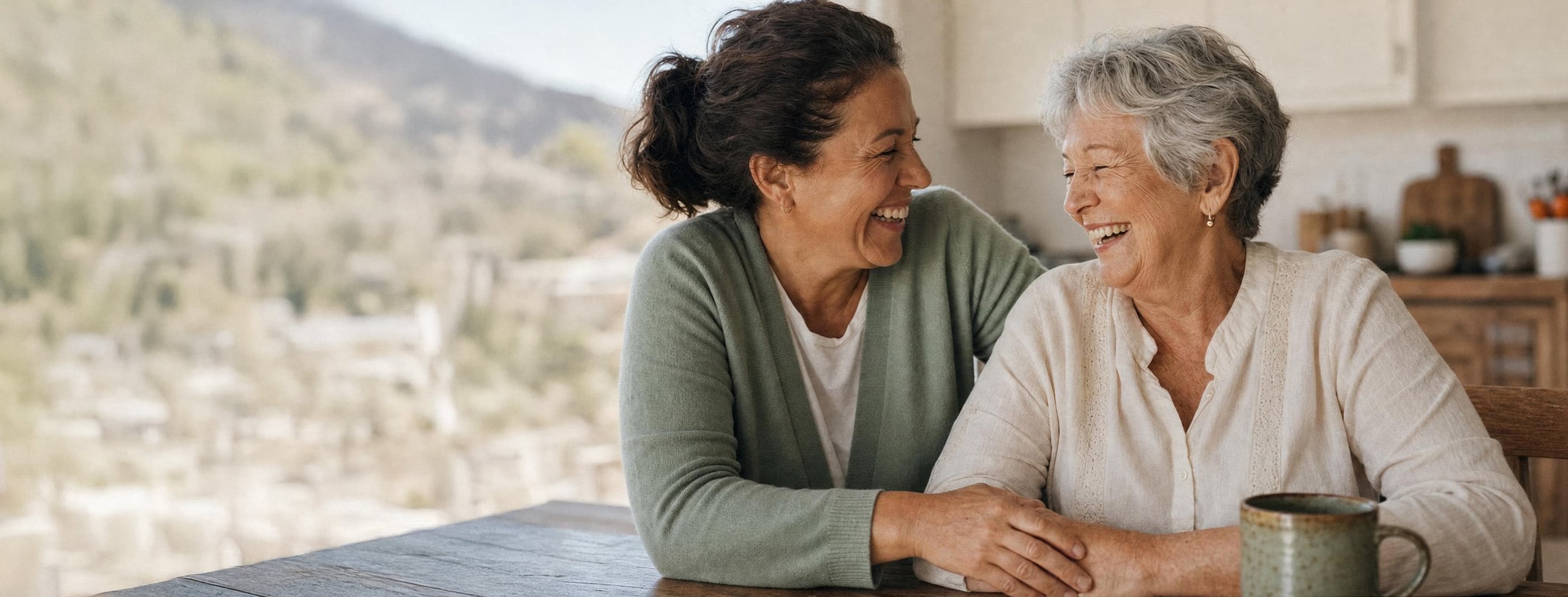 Ativo caregiver and senior sharing a warm laugh together at home in a sunlit kitchen